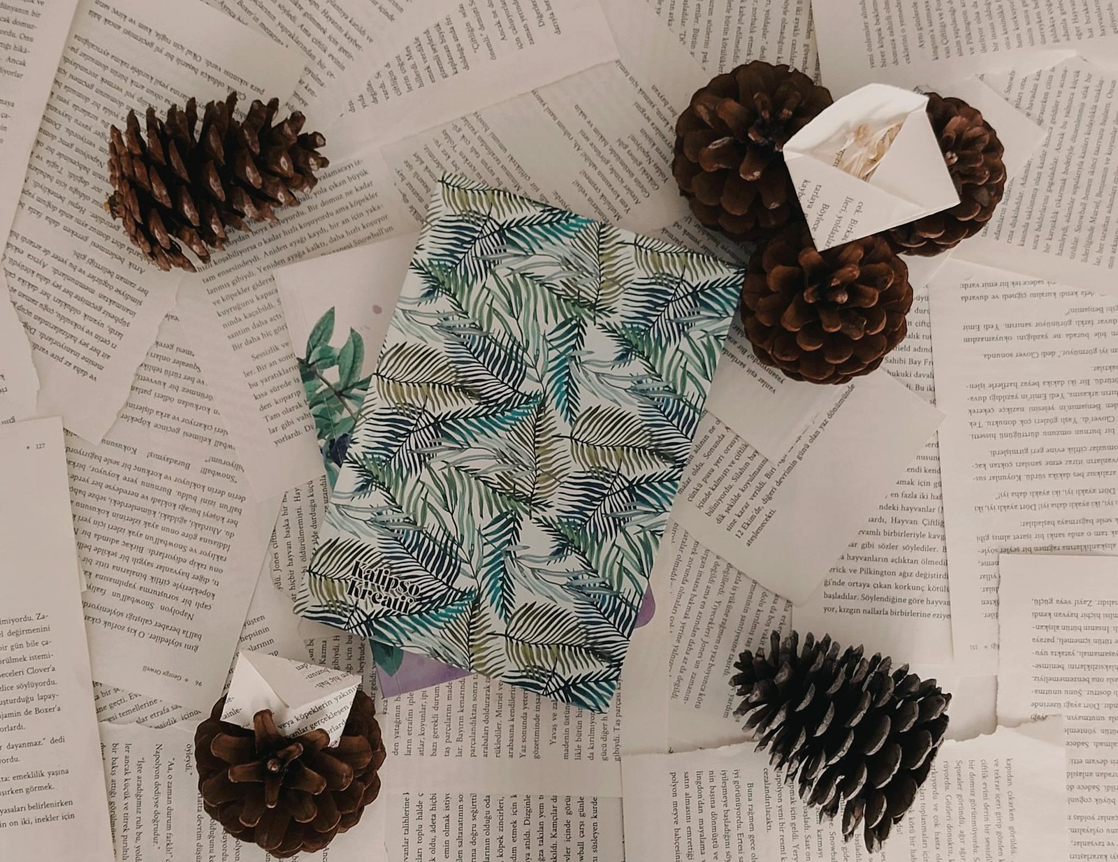 A beautifully wrapped present with leaf patterns surrounded by scattered book pages and pine cones.