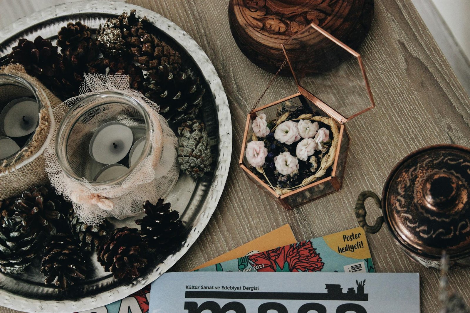 Cozy rustic decor featuring pinecones, glass jars with candles, and vintage elements on a wooden surface.